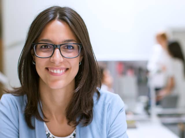 Young woman in glasses and light blue sweater in office setting.