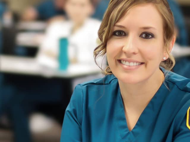 Young woman in classroom, all in blue scrubs.