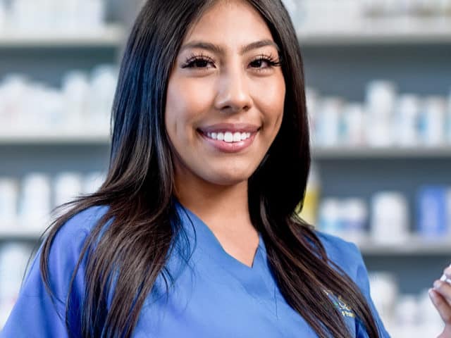 Young woman in blue scrubs in pharmacy setting.