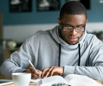 Focused millennial college student making notes while studying in cafe